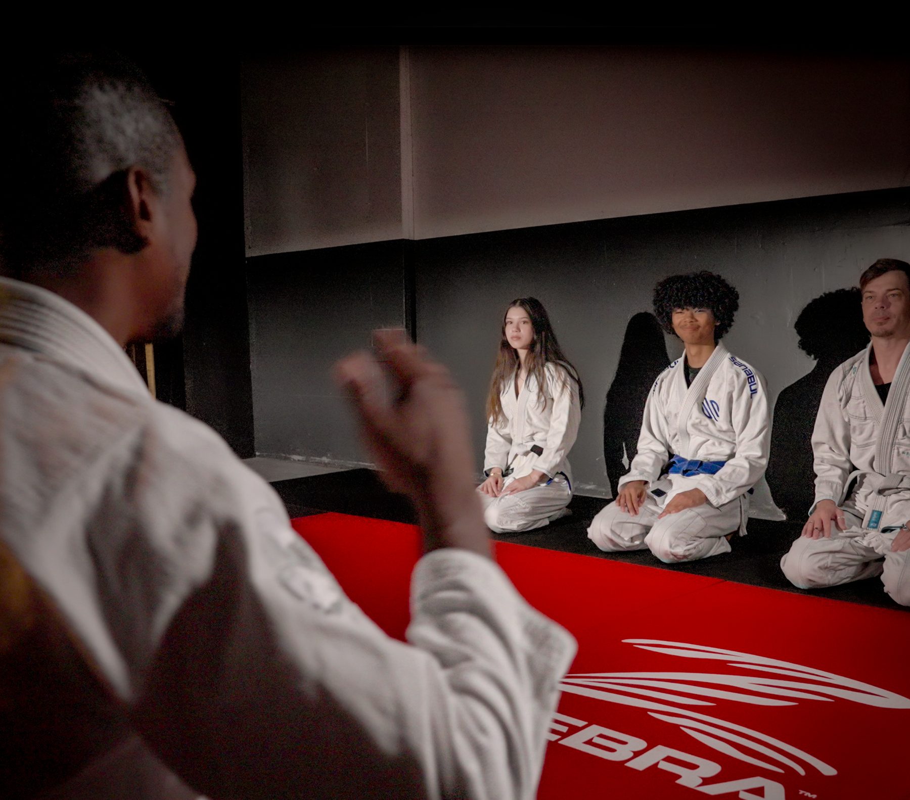 Coach teaching three students kneeling on the mats during class